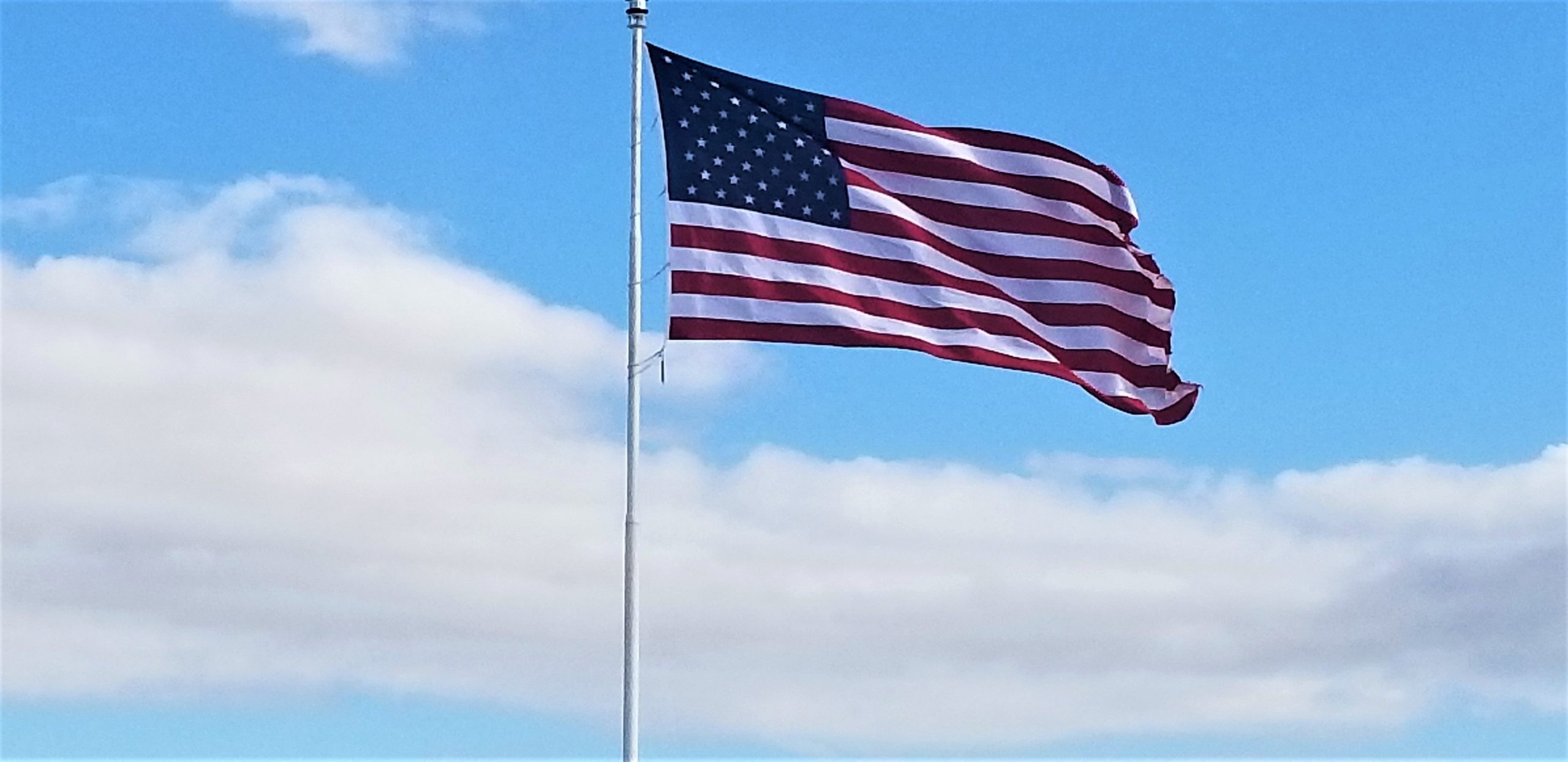 American flag waving in the sky with clouds in the background.